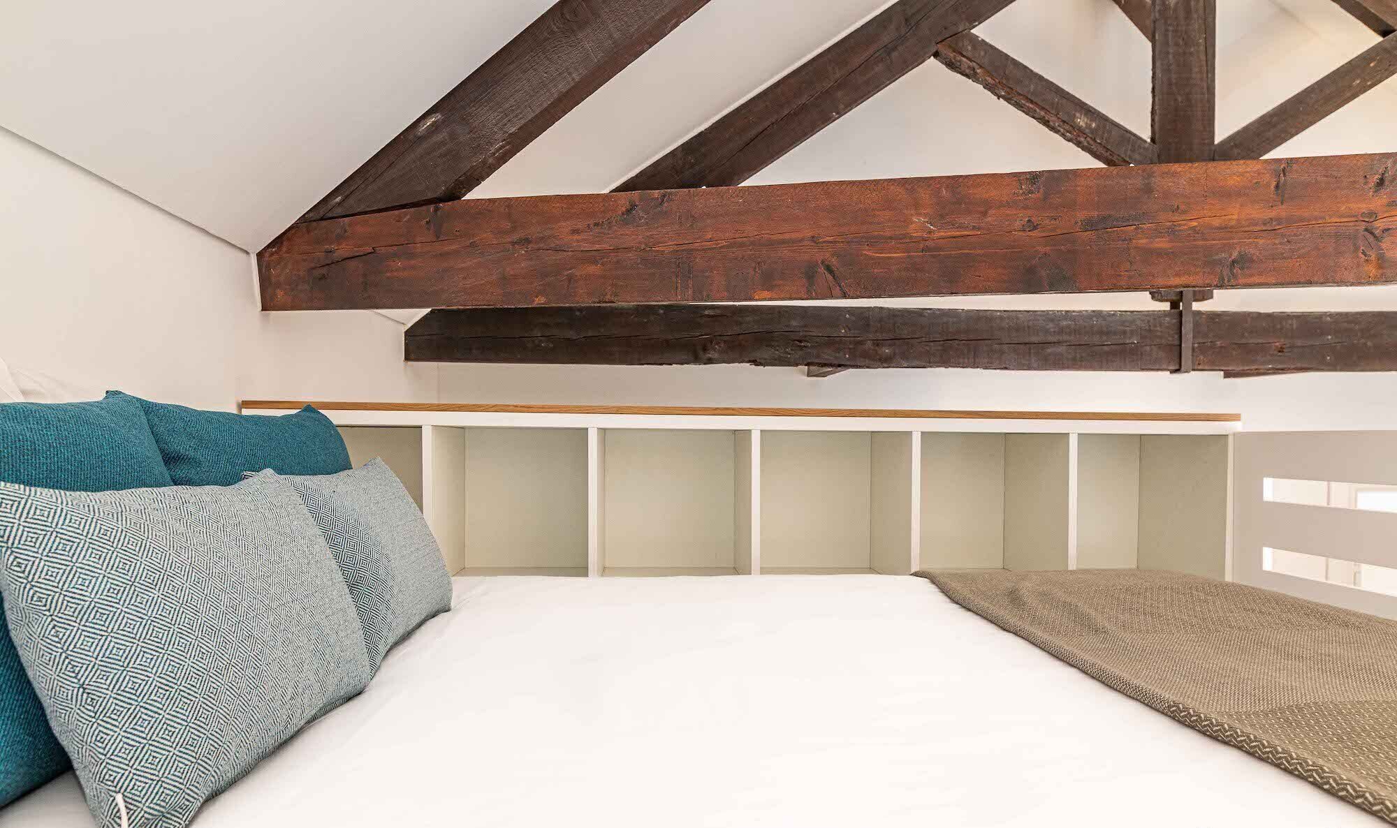 Una camera da letto con soffitto spiovente, travi in legno, un letto con cuscini decorati e un comodino.