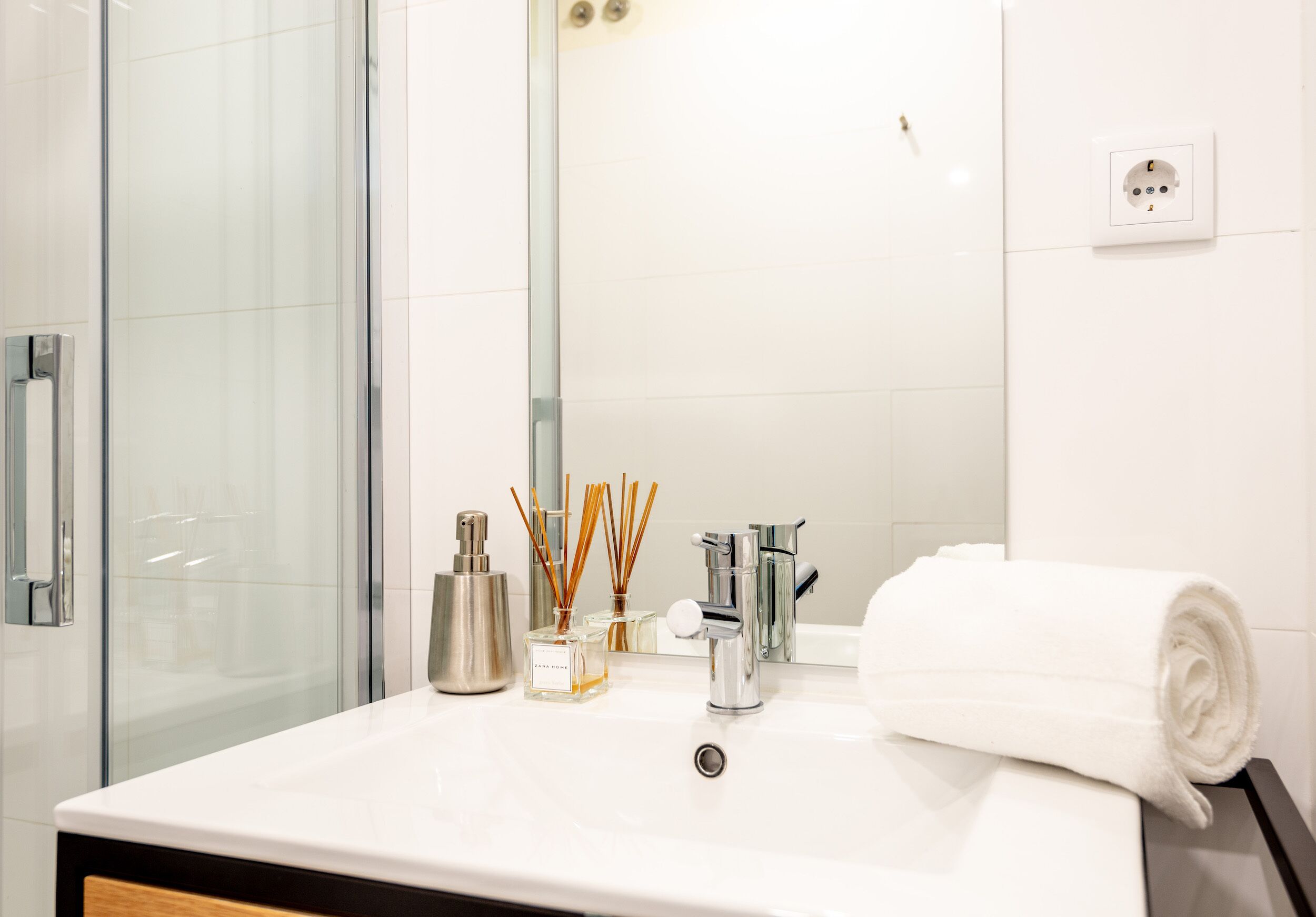 A bathroom with a white sink, a mirror, a towel, and a glass shower enclosure.
