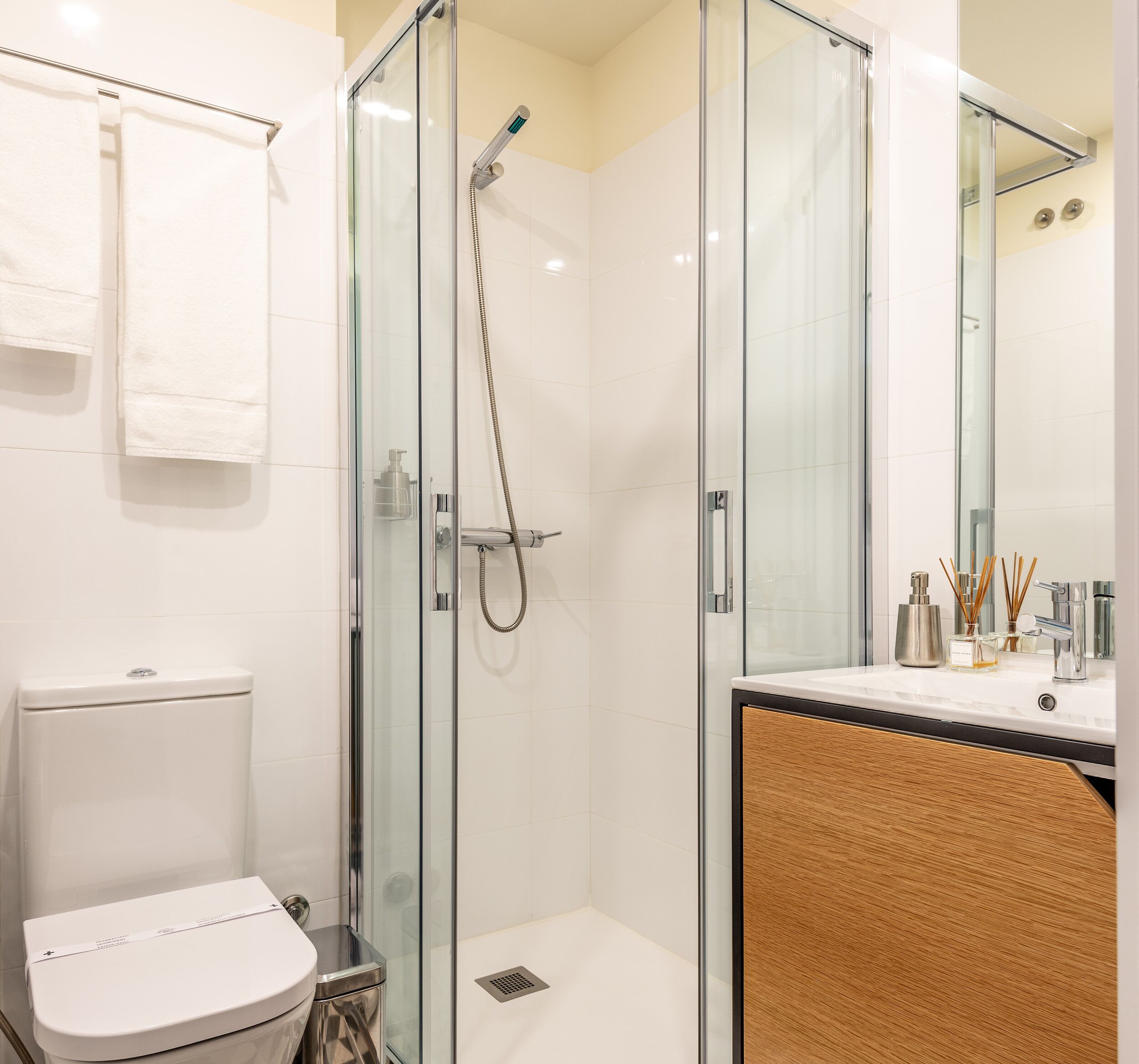 Un baño moderno con ducha de mampara de vidrio, inodoro blanco y tocador con espejo.