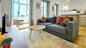 A modern living room with a grey sofa, a small round table, and a television on a wooden stand.