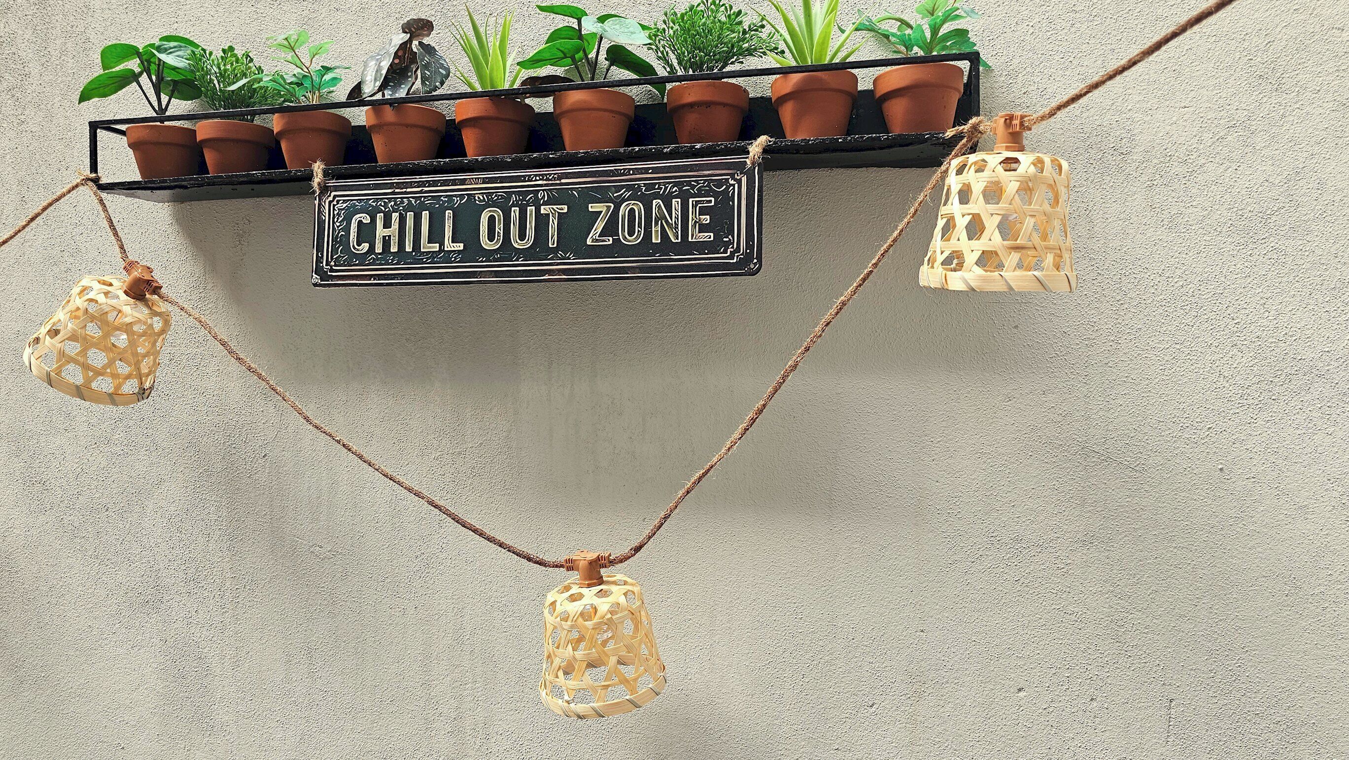 Ein an der Wand befestigtes Schild mit der Aufschrift "CHILL OUT ZONE", umgeben von Topfpflanzen und hängenden Laternen.