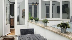 A patio area with a table and chairs, potted plants, and a sliding glass door leading to a room.