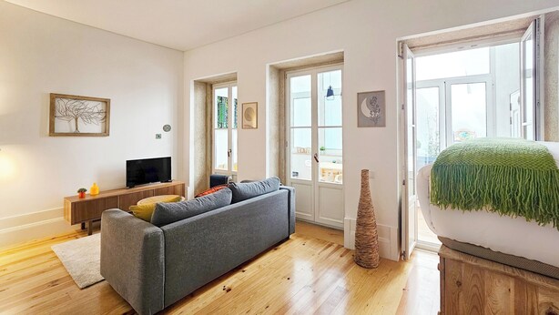 A living room with a grey sofa, wooden floor, and a television on a wooden stand.