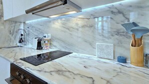 A kitchen with a marble countertop, a built-in oven, a range hood, and a wooden utensil holder.