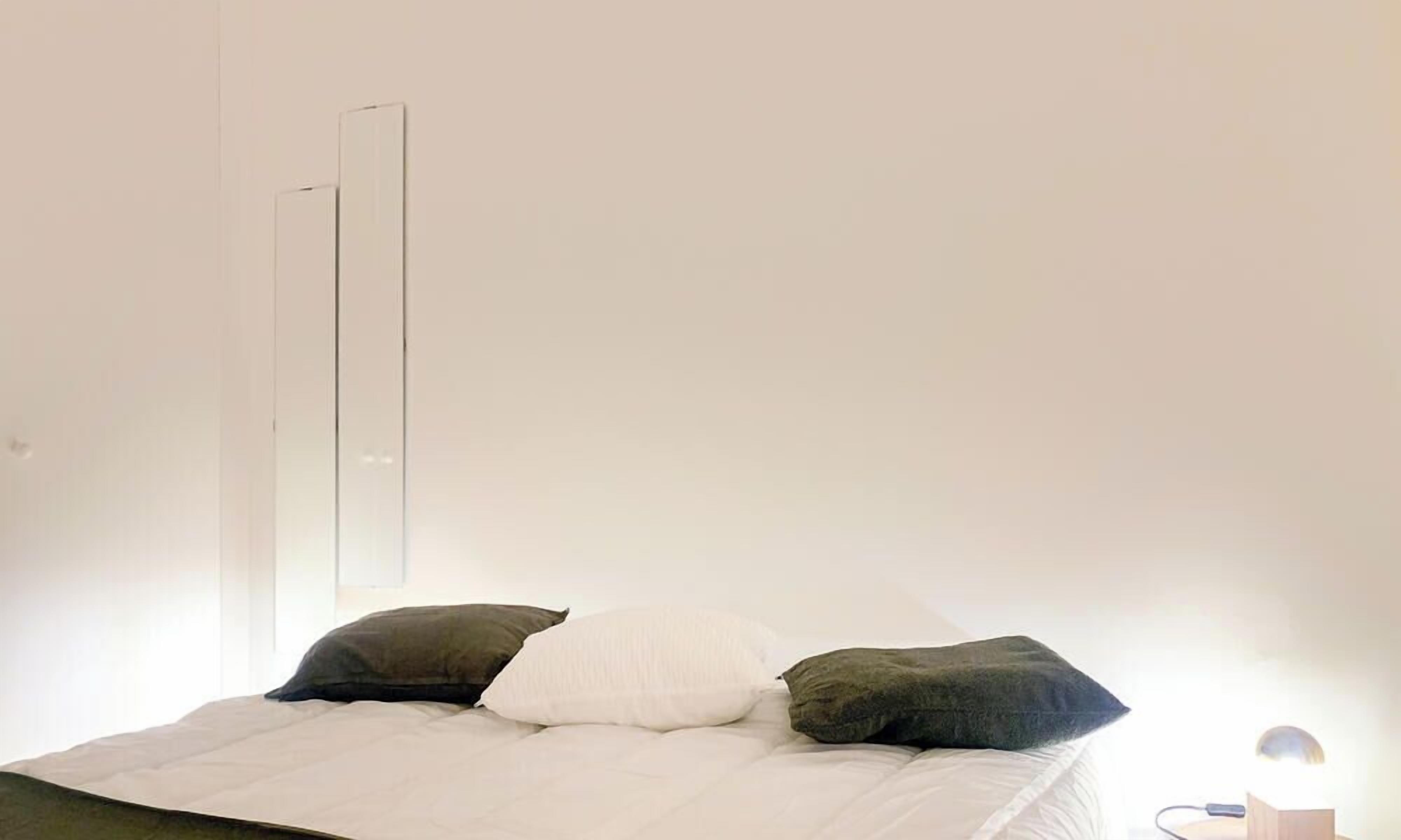 A minimalist bedroom with a bed, a bedside lamp, and a mirror on the wall.