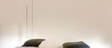 A minimalist bedroom with a bed, a bedside lamp, and a mirror on the wall.