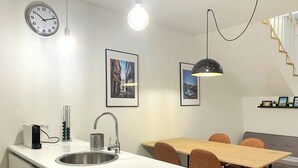 Eine moderne Küche mit weißer Arbeitsplatte, Spüle aus Edelstahl und einem Wasserkocher. Es gibt einen Essbereich mit Holztisch und Stühlen sowie eine Treppe mit Holzgeländer.