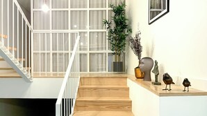 Eine Treppe mit Holzstufen und weißen Geländern führt zu einem Raum mit großen Fenstern und einer Pflanze.