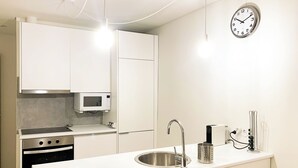 Eine moderne Küche mit weißen Schränken, einer Edelstahlspüle, einer Mikrowelle und einer Uhr an der Wand.