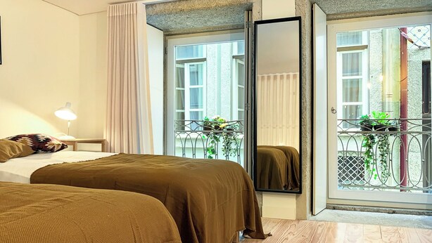 Ein Hotelzimmer mit zwei Betten, einem Nachttisch mit Lampe, einem großen Spiegel und einem Balkon mit Pflanzen.