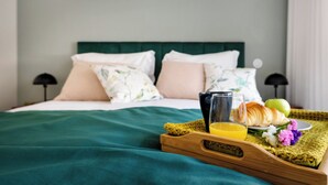 En pænt redt seng med et grønt lagen, en bakke med croissanter, et æble og et glas appelsinjuice.