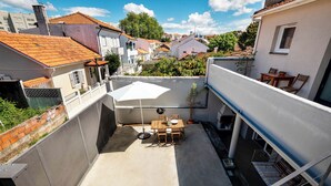 Um terraço no telhado com uma mesa e cadeiras, rodeado por edifícios.
