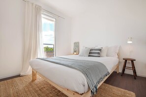 A bedroom with a bed, a nightstand, a lamp, a window with curtains, and a view of greenery outside. - Aguda1 · Aguda's Family House 4bd, Parking, BBQ (Porto)