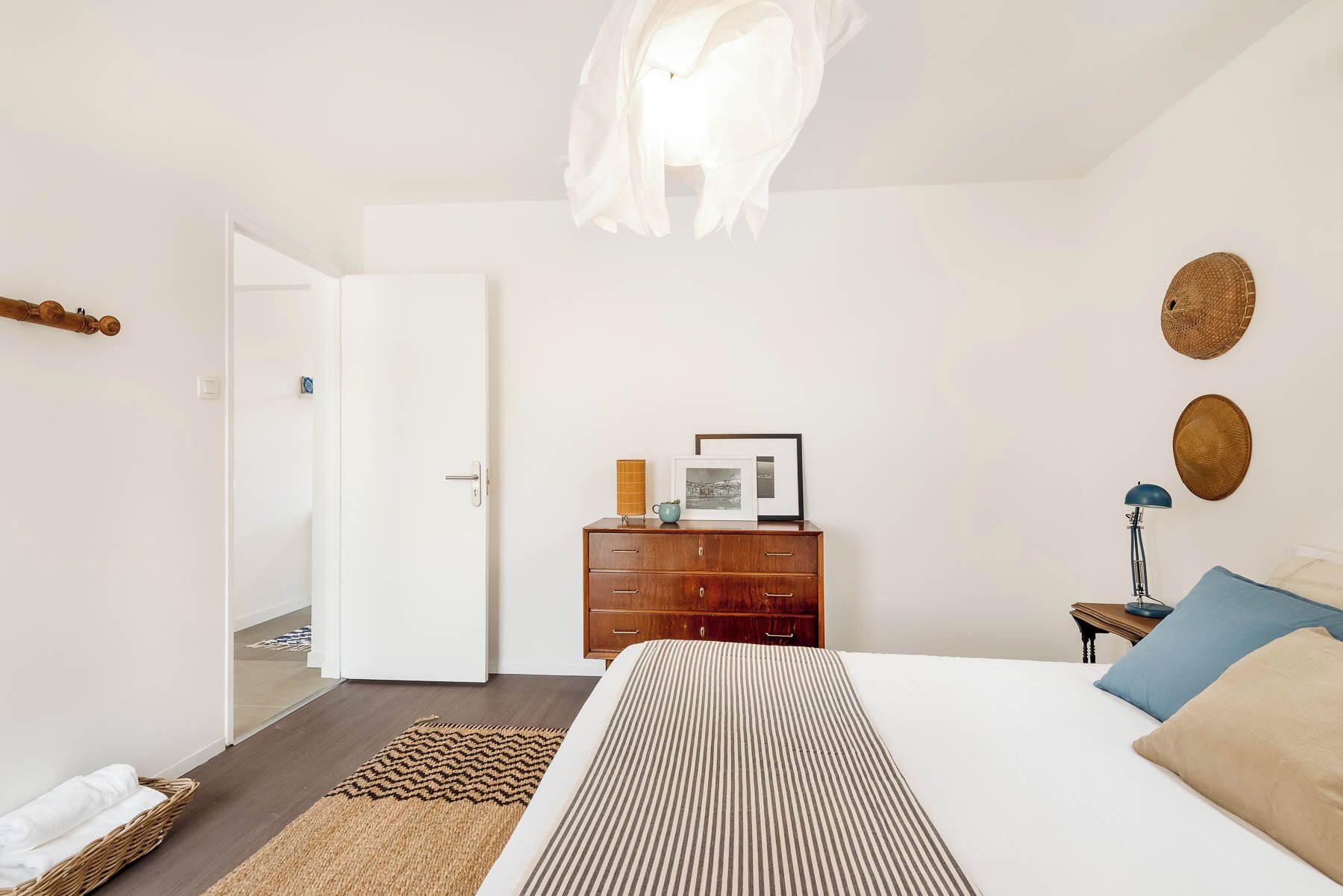 Un dormitorio con una cama, un aparador de madera, una mesita de noche, una lámpara y una lámpara colgante.