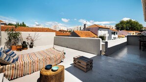 Terraço no telhado com tapete estampado, um banquinho de madeira e um banco.
