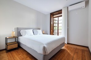 Un dormitorio moderno con cama, mesitas de noche y un equipo de aire acondicionado.
