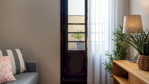 A room with a dark wooden door, a grey sofa with striped pillows, a small potted plant, and a lamp on a wooden console table. - Rivol2 · Wonderful 1BR Next to Rivoli Theatre (Porto)