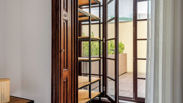 A room with a wooden bookshelf, a small table with a lamp, and a sliding glass door leading to an outdoor area with a tiled floor and greenery. - Rivol2 · Wonderful 1BR Next to Rivoli Theatre (Porto)