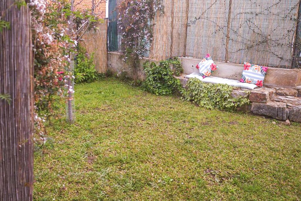 Un patio trasero con césped, cerca de madera, un banco de piedra y una pequeña zona ajardinada.