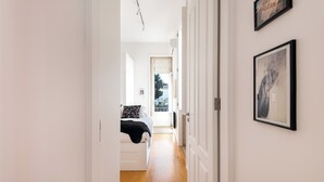 A narrow hallway leading to a bedroom with a bed and a door. - Markes · 🪴 Lovely 1BR Home w/ Sunny Backyard (Porto)