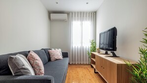 Ein modernes Wohnzimmer mit einem grauen Sofa, einem TV-Schrank aus Holz und einem großen Fenster mit transparenten Vorhängen.