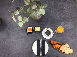 A breakfast setup with a plate of croissants, a cup of coffee, a glass of orange juice, and two small dishes with jam and butter on a dark surface. - Acm031 Gallery 92 2BD Duplex +balcony (Porto)