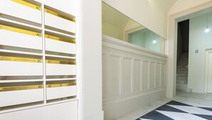 A hallway with a white wall, numbered storage units, a marble floor, and a staircase. - Prt002 · Charming 1 bed +1 @ Avenida dos Aliados (Porto)