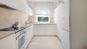Una cocina moderna con armarios blancos, horno integrado, estufa y refrigerador.