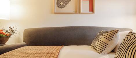 A neatly made bed with patterned pillows, a grey headboard, and a framed abstract artwork on the wall.
