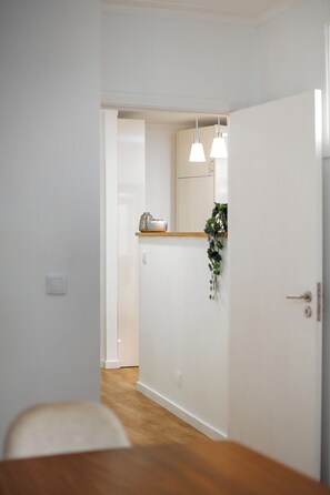 A hallway with a wooden floor, white walls, a door, and a small shelf with a plant. - Gaia23 · Lovely 2-bed w/ Parking Amazing View (Vila Nova de Gaia)
