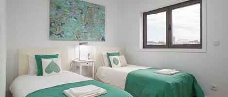A hotel room with two beds, a window, a painting, and a nightstand.