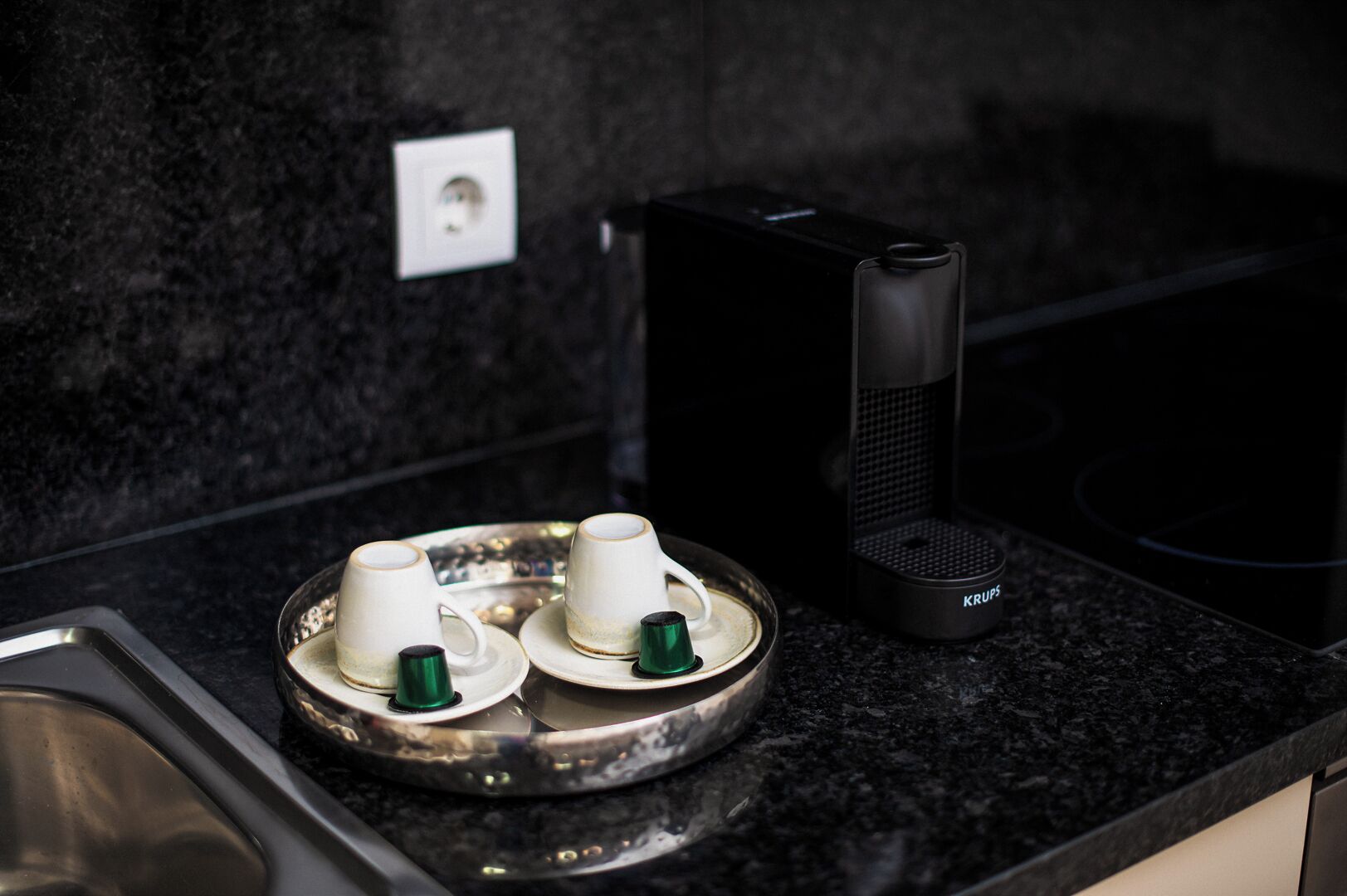A kitchen counter with a coffee maker, two cups, and a tray.