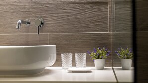 A bathroom with a large white sink, two glass tumblers, and two potted lavender plants on a white countertop.