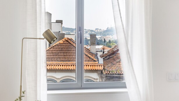 A room with a large window, white curtains, a bed, and a lamp.