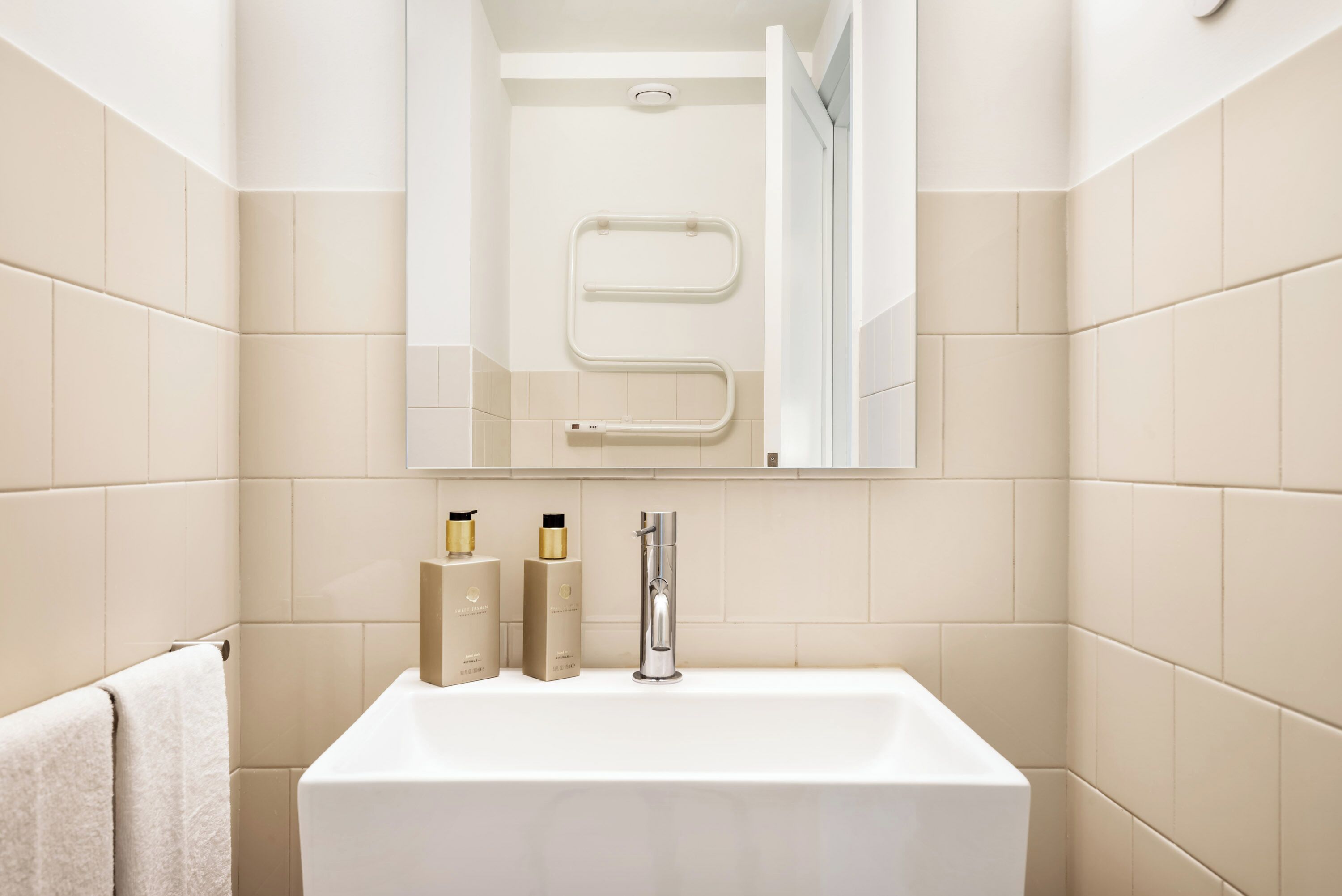 A modern bathroom with a white sink, a mirror, and two toiletry bottles on the counter.
