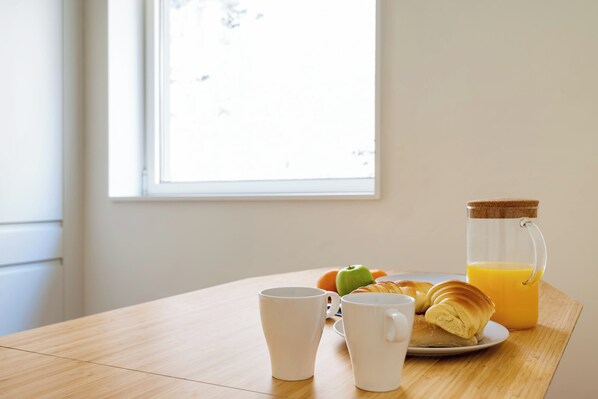 A breakfast table with croissants, a jug of orange juice, and two white mugs.