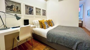 A bedroom with a bed, a desk with a chair, a lamp, and framed pictures on the wall. - Santo1 · Modern Studio Close to Timeout Market (Lisbon)