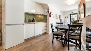 Una cocina moderna con armarios blancos, salpicadero verde y un comedor con mesa y sillas redondas.
