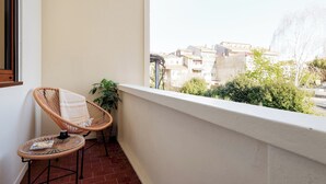 Ein Balkon mit Korbstühlen, einem kleinen Tisch und Blick auf Häuser und Grünflächen.