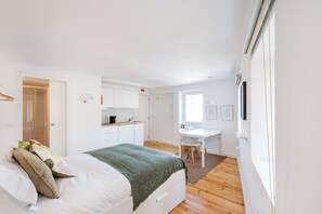 A modern bedroom with a bed, a desk, and a kitchenette.