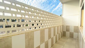 Un balcone con pavimento a scacchi, una parete bianca con motivo a griglia e vista sul cielo.