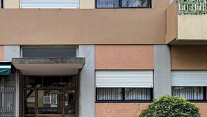 Un edificio a più piani con facciata lineare, ampie finestre dotate di persiane e un ingresso con cancello.