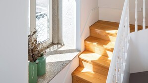 Un escalier avec des marches en bois menant à un palier, une fenêtre donnant sur la rue et un tableau encadré accroché au mur.