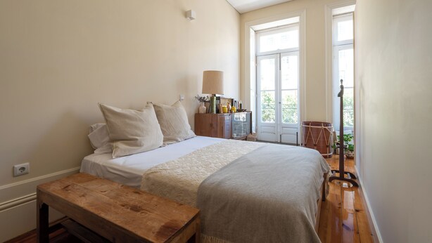 A bedroom with a bed, a wooden bench, a dresser, and a window with a view of greenery. - Urbsc3 · Santa Catarina Studios · Apt 3 (Porto)