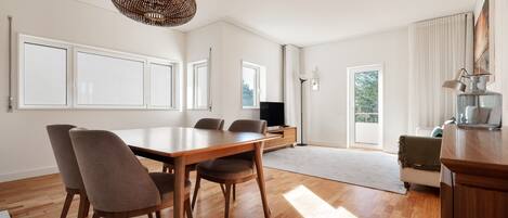 Un comedor amplio con una mesa y sillas de madera, una lámpara colgante tejida y ventanas grandes que dejan entrar luz natural.