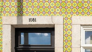 En dubbeldörr med en numrerad platta ovanför, där siffran "1081" står, placerad i en mur av sten med ett mönstrat kakel.
