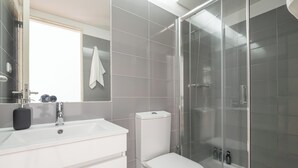 A modern bathroom with a white sink, toilet, and glass-enclosed shower.