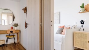 A modern bedroom with a white bed, a wooden desk, a chair, a mirror, and a bedside table with a lamp. - Herois · Lovely 2-bed in the City Centre (Porto)