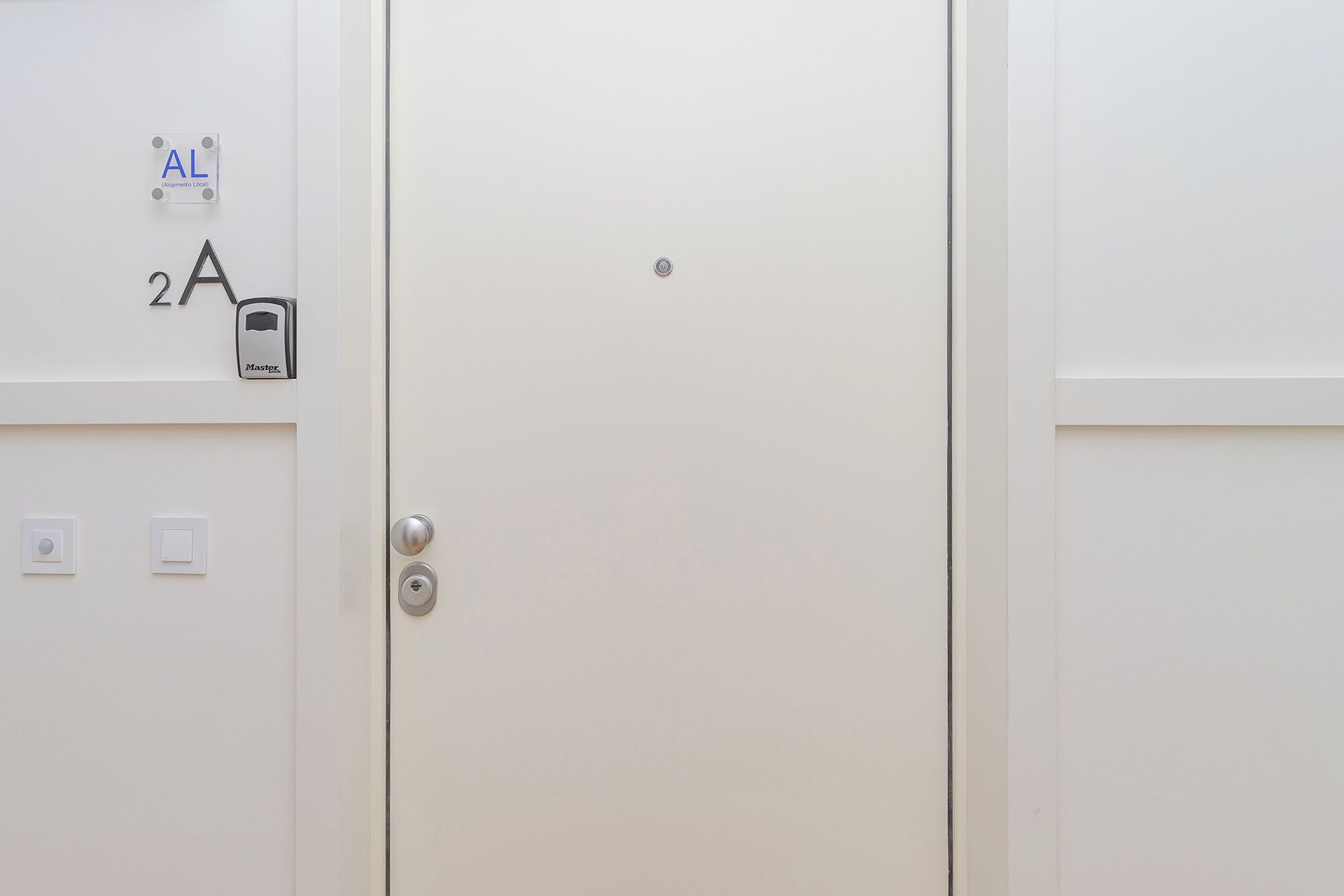 A white door with a keypad lock, a small circular device, and a label reading "AL (Alquiler Local)".