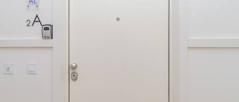 A white door with a keypad lock, a small circular device, and a label reading "AL (Alquiler Local)".